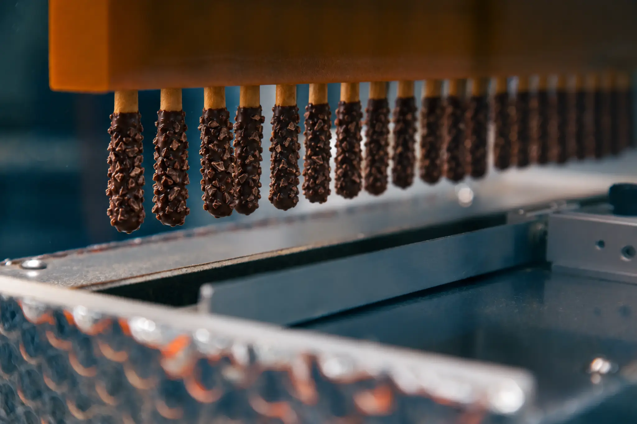 Robotic fixture holding a row of cylindrical cookies above the coating station